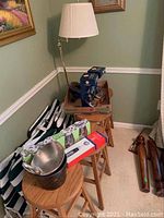 Four wooden stools, one floor lamp, some packed items and cushions arranged against wall