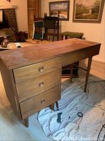 Full view of the wooden desk showing the top surface, drawers, and tapered legs. Visible wear and damage on the top surface.