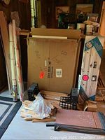 Framing supplies with wooden frame parts in crates, rolled canvas, vinyl roll, and stacked mat boards in a cardboard container