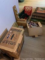 Lot showing boxed image projector, red milk crate, boxes and bags with pennants and other items arranged on floor.