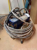 Full view of the Duron Performance 395 electric paint sprayer with hoses coiled around the unit on a small stool.