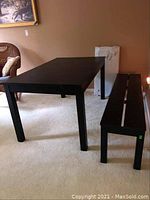 Photo of black IKEA table and matching bench seat in room with beige carpet and tan walls, showing wear and overall design