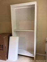 Front view of the white wooden bookshelf section with two removable panels leaning against it.