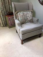Side angled view of wingback armchair with decorative pillow showing upholstery pattern and wooden legs.