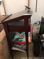 Side view of the wooden podium showing the slanted top, middle shelf with fabric items, and bottom drawer.