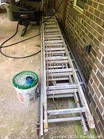 Two aluminum extension ladders laid flat on ground, showing full length with pulley ropes visible.