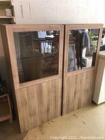 Pair of matching wood veneer cabinets with glass upper doors and solid lower doors shown front-facing