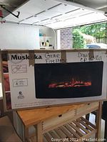 Boxed Muskoka brand electric fireplace showing front view of unit and packaging labeled with product features including remote control and heating capacity up to 400 sq ft.