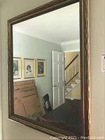 Framed wall mirror showing wood grain frame and reflected room including door, chairs, and wall art.