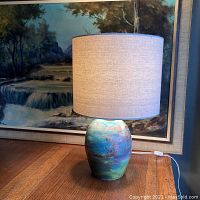 Full view of the handmade raku pottery lamp with linen-shade on wooden table.
