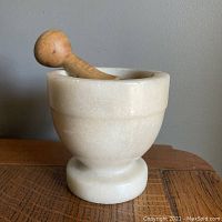 Side view of marble mortar with wooden pestle inside, showing mortar's rounded shape and creamy patina.