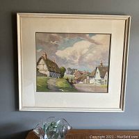 Overall view of the framed watercolour print showing the village scene under cloudy sky with thatched cottages.