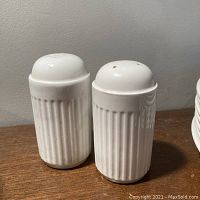 Photo showing front view of the pair of white ironstone salt and pepper shakers with fluted design standing on wooden surface.