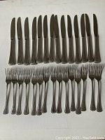 Top view showing 14 knives and 15 forks arranged side by side on white background.