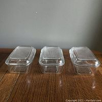 Three clear rectangular glass containers with lids placed side-by-side on a wooden surface, viewed from above.