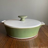 Side view of the olive green casserole dish with white lid and knob on top, showing the dish's shape and handles.