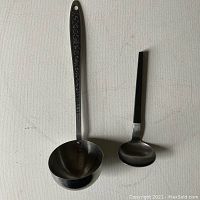 Photo showing two ladles side by side on a neutral background, one with a decorative handle and one with a plain black handle