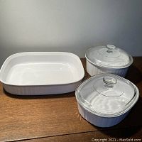Group of three Corning Ware French White casserole dishes, two with glass lids and one without lid, showing sizes and shapes.