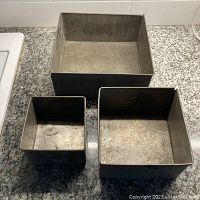 Top view of three square cake pans arranged from largest to smallest on counter showing inside surfaces.