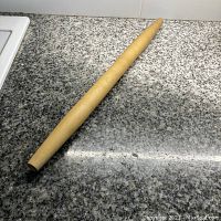Wooden tapered rolling pin lying on a gray speckled countertop, showing full length and tapering shape.