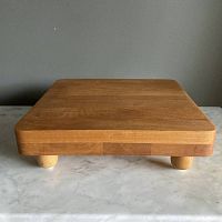 Front view of the square footed wooden cutting board showing smooth wood grain surface and rounded edges.