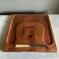 Top-down view of wooden cheese board showing recessed areas for cheese and crackers, with cream handled cheese knife resting in recess.