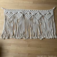 Macramé wall hanging full view laid flat on wood floor showing width and fringe length.