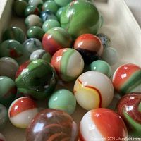 Close-up image showing a variety of marbles in rusts, greens, and whites with distinct swirls and glossy finish.