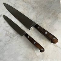 Two J. A Henckels chef's knives with wooden handles and metal rivets, one with a 6-inch blade and one with an 8-inch blade, showing wear.