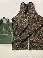Full view of floral patterned apron with PVC coating and Harrods shopping bag beside it for size reference.