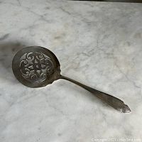 Full view of the vintage tomato spoon server showing the round pierced bowl with ornamental cutouts on a marble surface.