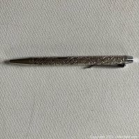 Full view of the slender silver ballpoint pen with intricate Hebrew tribal symbol engravings along the barrel.