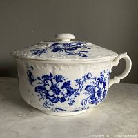 Full side view of antique white ironstone chamber pot with blue floral transferware pattern and lid. Shows handle and embossed scrollwork.