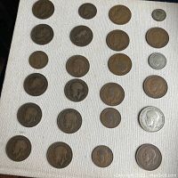 Top-down image showing 29 British coins laid out on white cloth, displaying heads side with portraits of King George V and King George VI