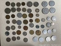 Full layout showing approximately 50 international coins arranged in rows on cream fabric background.