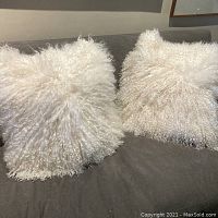 Pair of white Mongolian lamb pillow covers displayed on a gray couch showing curly lamb fur texture.