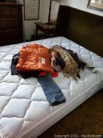 Pile of women's clothing including jeans, orange vest, sweaters, and shawls.