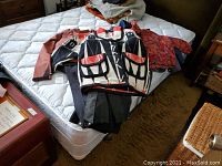 Four items of ladies outerwear laid on a bed: long black sheepskin coat, patterned jacket, rust-colored Columbia softshell jacket, and black snow pants.