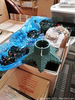 Overview of Christmas tree stand, several bags of string lights, tinsel garland, and napkins on table.
