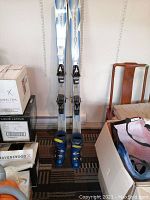Full view of skis standing upright with ski boots placed in front, showing overall lot