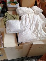 Full view of white goose down filled duvet alongside packaged bed sheets and bedding items, showing condition and quantity.