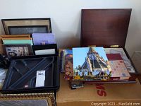 Lot contains a variety of small framed pictures, wooden letter caddy parts, notebooks, Scrabble game box, jigsaw puzzle box, and wooden chest containing marbles and fine stationery.