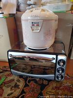 White National brand rice cooker with pink floral design sitting on top of black Delonghi toaster oven with control dials visible