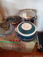 Calphalon frying pan, stainless pasta pot, porcelain casserole and glass serving dishes grouped on top of a box