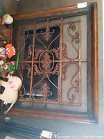 Full view of the large burnished metal wall art featuring scrolls and leaves in a wooden frame, surrounded by stuffed toys not included in lot.