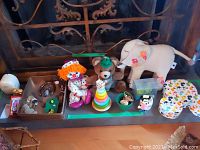 Photo showing the lot on a wooden surface. Includes elephant stuffed animal with floral embroidery, bear plush with green hat, clown doll, Mickey Mouse box, Minnie toothbrush holder, toddler puzzle, clock, wristwatch, and figurines.