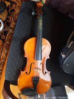 Half size Suzuki violin lying on black surface showing wood finish, f-holes, fingerboard and tailpiece