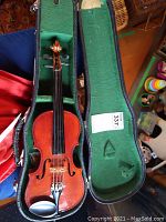 Full violin in open black case with green felt lining, visible wear on case and violin.