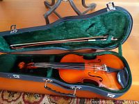 Opened violin case showing Suzuki 1/4 size violin with bow inside, green plush interior liner visible.