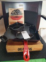 Antique Japanese cast iron pans displayed on a chair, showing red handled frying pan, raclette pan, instruction sheet and original box.